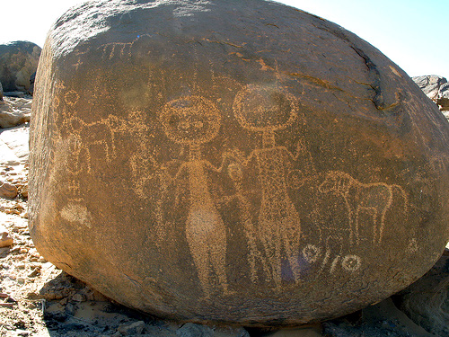 boulder petroglyph of women with arms raised, animals