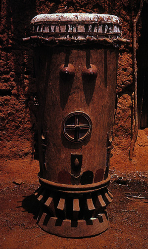 tall wooden drum with carved breasts and vulva