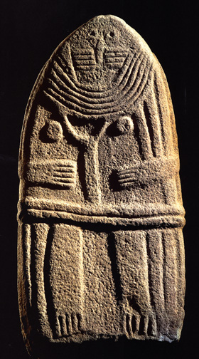 oval stone relief of woman with multiple necklaces, breasts, belt, holding a Y-shaped object in her hands